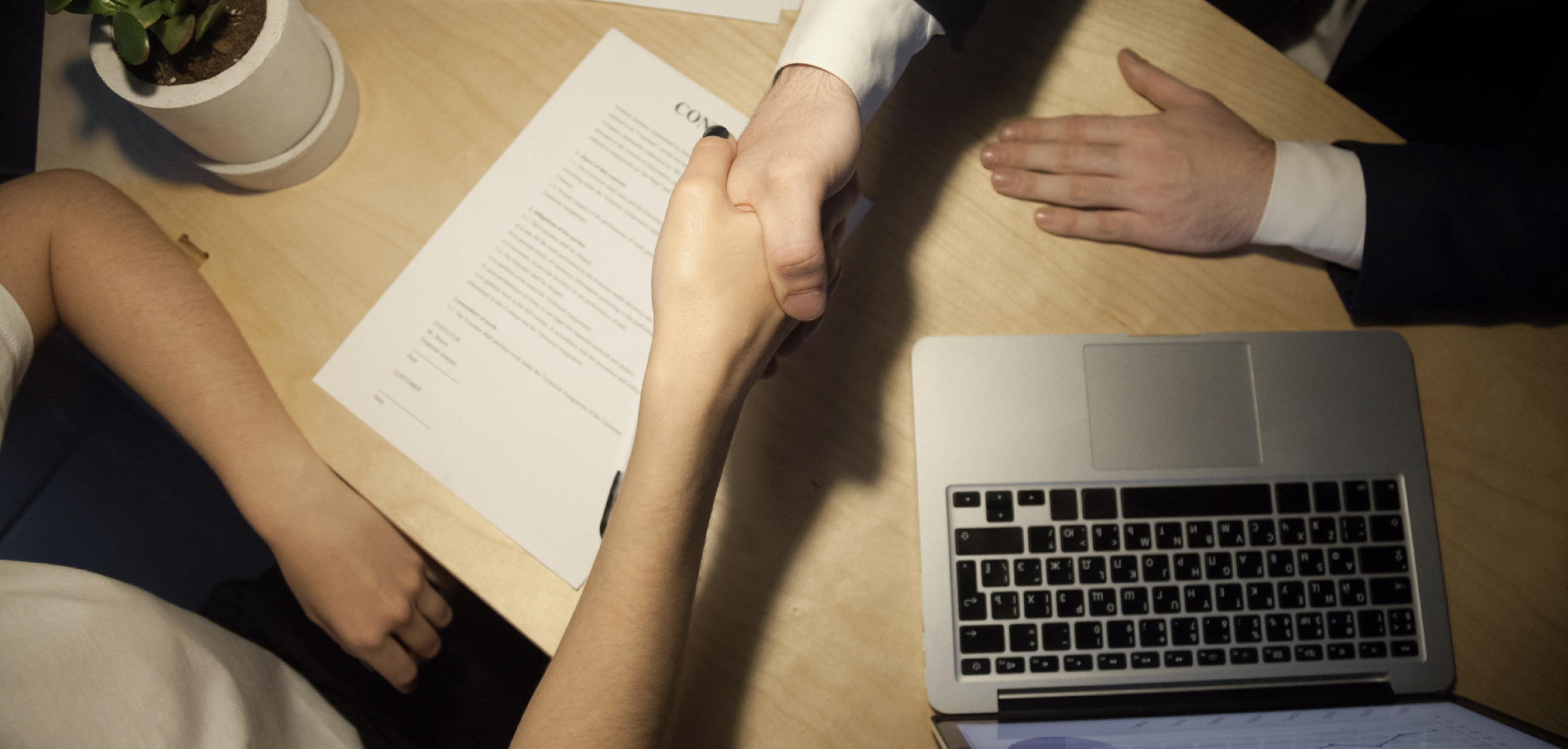 Dos personas estrechándose las manos sobre un contrato, en señal de acuerdo institucional